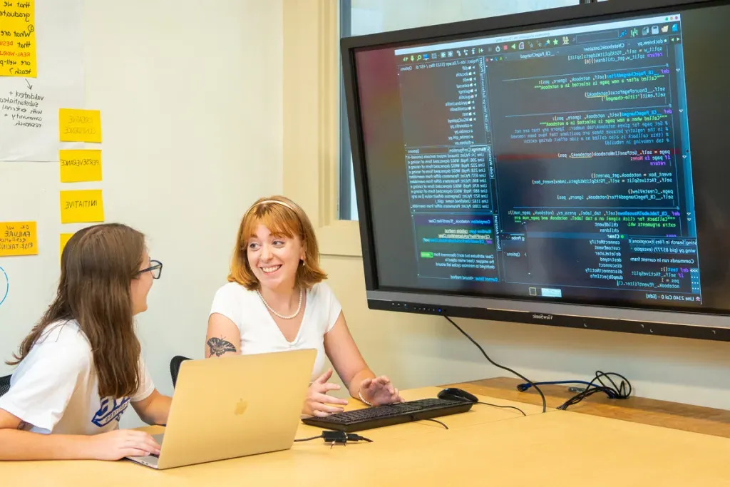 Two students review computer programming code on a large monitor